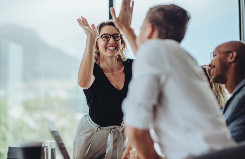 Business damen gjør high five til mannlig kollega i et styrerom.
