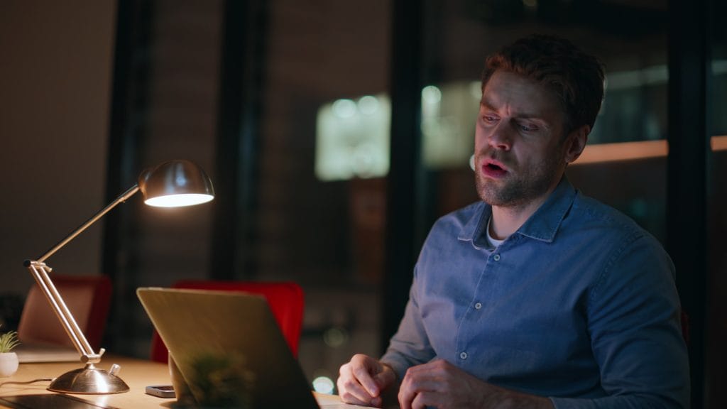 Frustrert B2B-selger som jobber sent på hjemmekontor ved laptop, stresset fordi han ikke får lukket salget (closing).